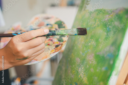 close-up art student's hand using watercolor paint brush painting on canvas doing some art projects on studio workshop