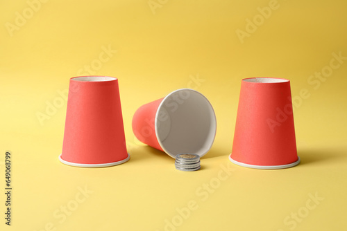 Three red cups and coins on yellow background. Thimblerig game photo