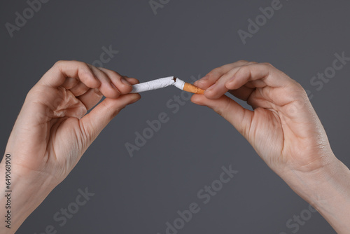 Stop smoking concept. Woman breaking cigarette on gray background, closeup
