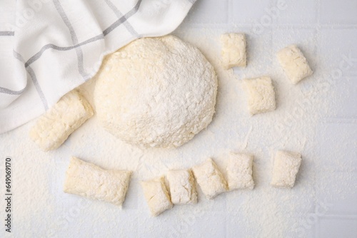 Making lazy dumplings. Raw dough and flour on white tiled table, flat lay