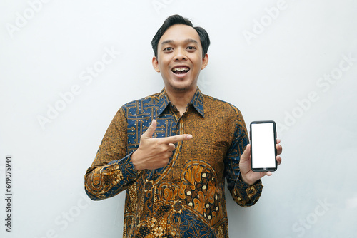 Portrait of Asian Indonesian man in Batik traditional shirt pointing to smartphone photo