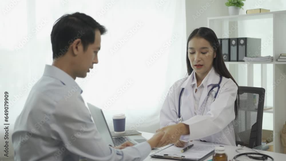 Asian female doctor in white uniform delivering good news Discussing results or symptoms and holding hands with male patient sitting at table in hospital health clinic. Asian female doctor in white uniform delivering good news Discussing results or symptoms and holding hands with male patient sitting at table in hospital health clinic.