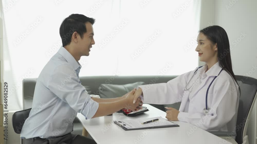 Asian female doctor in white uniform delivering good news Discussing results or symptoms and holding hands with male patient sitting at table in hospital health clinic. Asian female doctor in white uniform delivering good news Discussing results or symptoms and holding hands with male patient sitting at table in hospital health clinic.