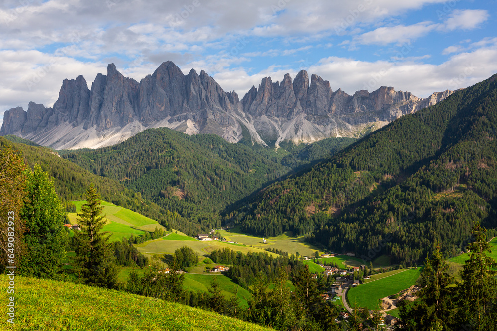 Fototapeta premium Breathtaking view of lush green Val di Funes valley with rustic cottages nestled amidst pristine alpine landscape against backdrop of rugged peaks 