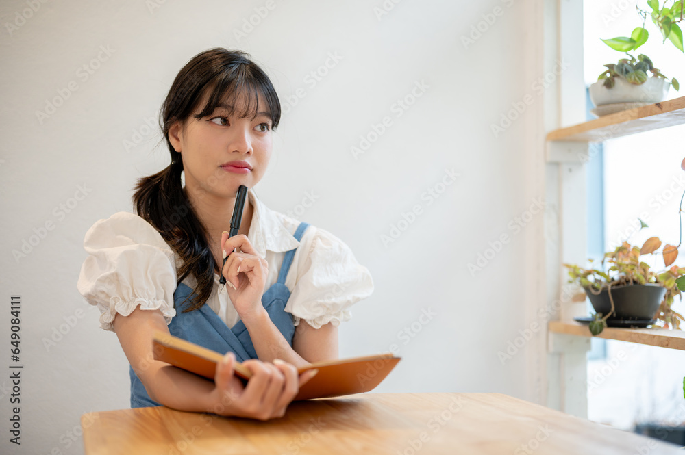 A pretty and thoughtful young Asian woman is thinking creative ideas, keeping her diary at a cafe A pretty and thoughtful young Asian woman is thinking creative ideas, keeping her diary at a cafe