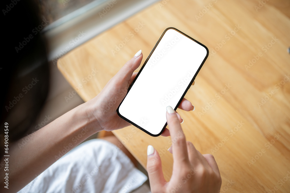 Close-up top view image of a woman holding a smartphone white screen mockup over a wooden table.