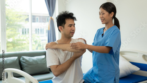 Handsome man exercising with dumbbells and stretching straps smiling in hospital department. Attractive nurse is helping him, orthopedic doctor helps do physical therapy, physical therapy in the clini photo