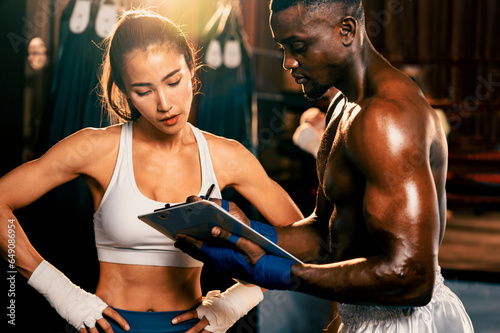 Asian female Muay Thai boxer and her personal boxing trainer discussing on her physical progress in the gym reflecting commitment to her body muscle growth and boxing performance. Impetus © Summit Art Creations