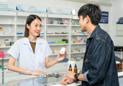 Pharmacist recommends medicines to customers.Taking the questions of medication. Asian female pharmacist giving prescription medications to customers at drugstore shelves.