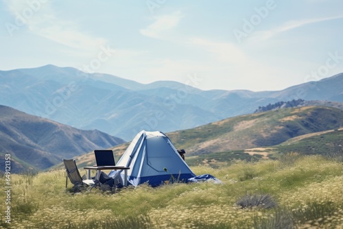 Laptop on a table next to a tent in a meadow, with mountains in the background, epitomizing the blend of work and leisure