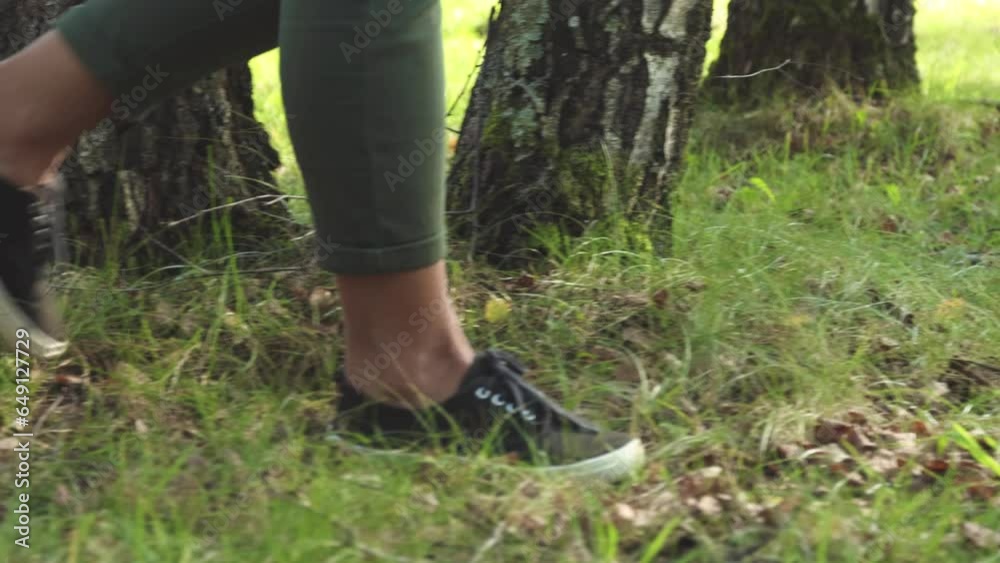 Close up of woman's legs wearing green pants and black shoes walking trough the park in early autumn season Close up of woman's legs wearing green pants and black shoes walking trough the park in early autumn season