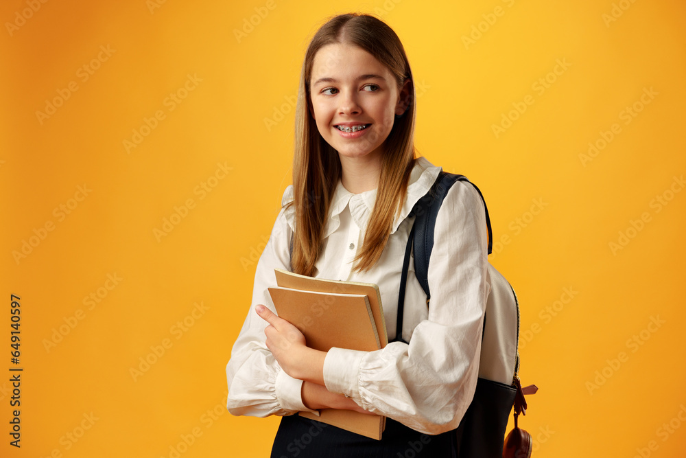 Teen girl in school uniform carry backpack on yellow background Teen girl in school uniform carry backpack on yellow background