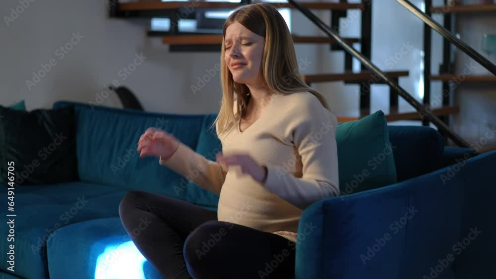 Side angle view exhausted pregnant young woman looking away having headache sitting at home on sofa. Portrait of tired Caucasian sad expectant with painful migraine and mood swings indoors