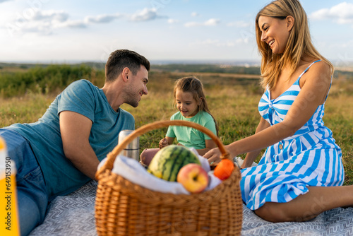 Parents and daughter have a picnic in the meadow, spend time together to bond and relax after a busy week