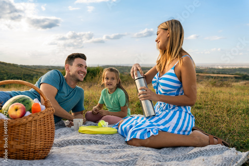 Parents and daughter have a picnic in the meadow, spend time together to bond and relax after a busy week