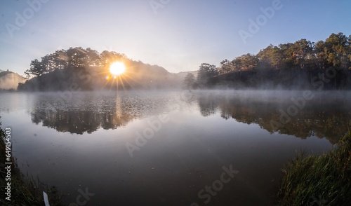 Dawn in the Golden Valley is shining through the pine hills, the sun shines on the foggy surface of the lake, the beautiful scenery of Da Lat