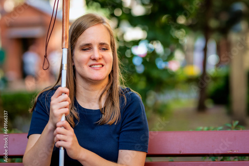 A visually impaired woman holding a white cane and sitting on a bench in the city photo
