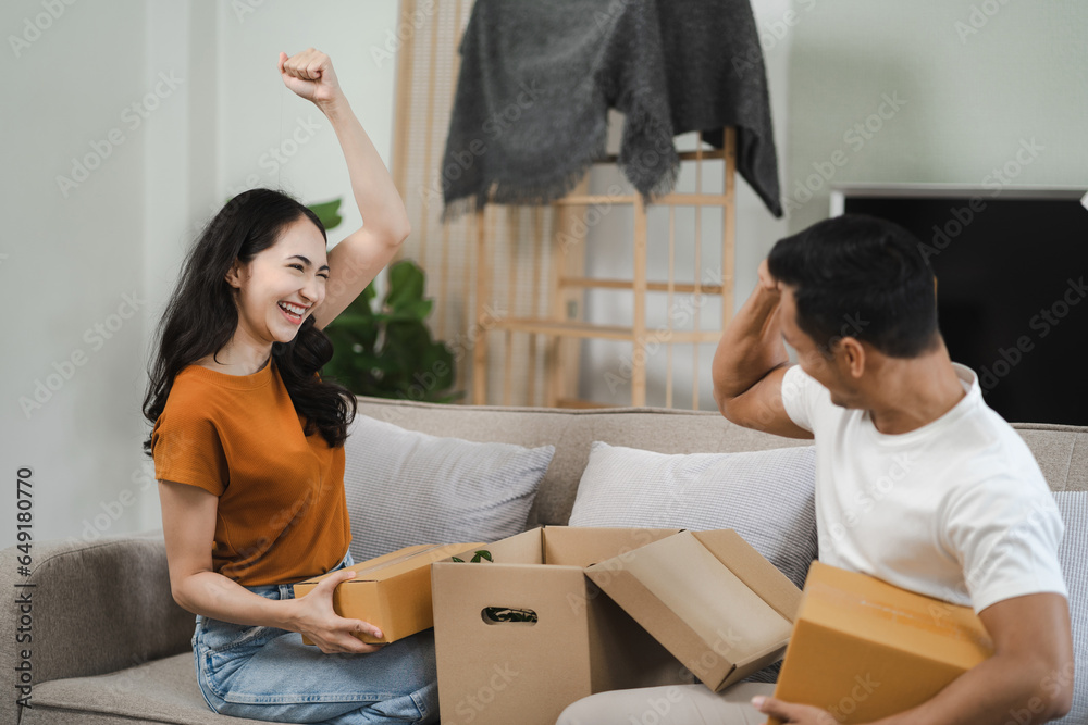 Successful young couple is moving to a nice new place, around boxes with their belongings. The room is very bright and bright, they are wearing casual clothes.