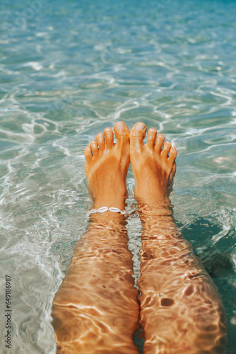 Tanned women's legs against the background of clear water. Stylish concept of leisure and travel.