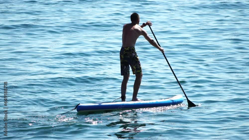 Man Sup Sea. Strong athletic man learns to paddle sup standing on board in open sea ocean on sunny day. Summer holiday vacation and travel concept. Aerial view. Slow motion