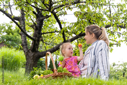 Girl showing apricot fruit to mother sitting on grass in garden photo