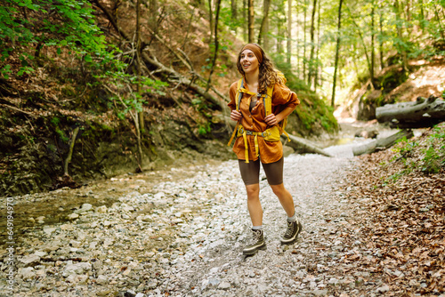 A traveler walks along a forest hiking trail in the mountains against the backdrop of mountain nature on a sunny day. Hiking, active lifestyle. Outdoor recreation concept.