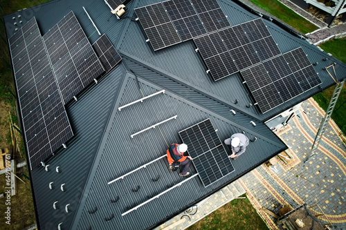 Engineers building photovoltaic solar module station on roof of house. Men electricians in helmets installing solar panel system outdoors. Concept of alternative and renewable energy. Aerial view.