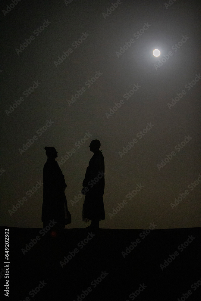 Buddhist monks standing under the moonlight during a zen retreat in the Sahara, Morocco.