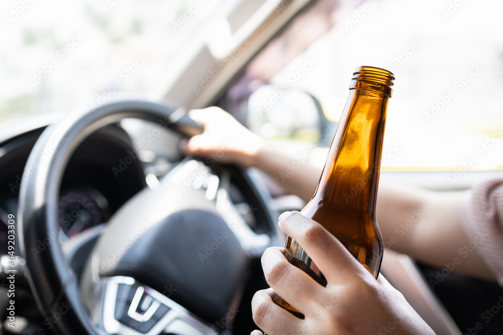 Intoxicated woman driver holding bottle of beer,asian female drinking alcohol while driving motor vehicle,risk or danger of road accidents,Campaign against drunk driving,Don't drink and drive concept - obrazy, fototapety, plakaty 