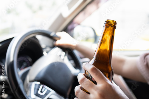 Intoxicated woman driver holding bottle of beer,asian female drinking alcohol while driving motor vehicle,risk or danger of road accidents,Campaign against drunk driving,Don't drink and drive concept photo