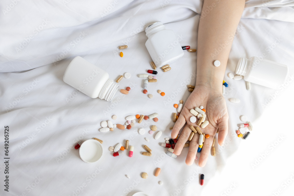 Different of pills tablets capsules,many drugs in hand of young woman,multicolored medicine scattered on her bed,concept of suicide by taking an overdose of a drug,World Suicide Prevention Day. - obrazy, fototapety, plakaty 