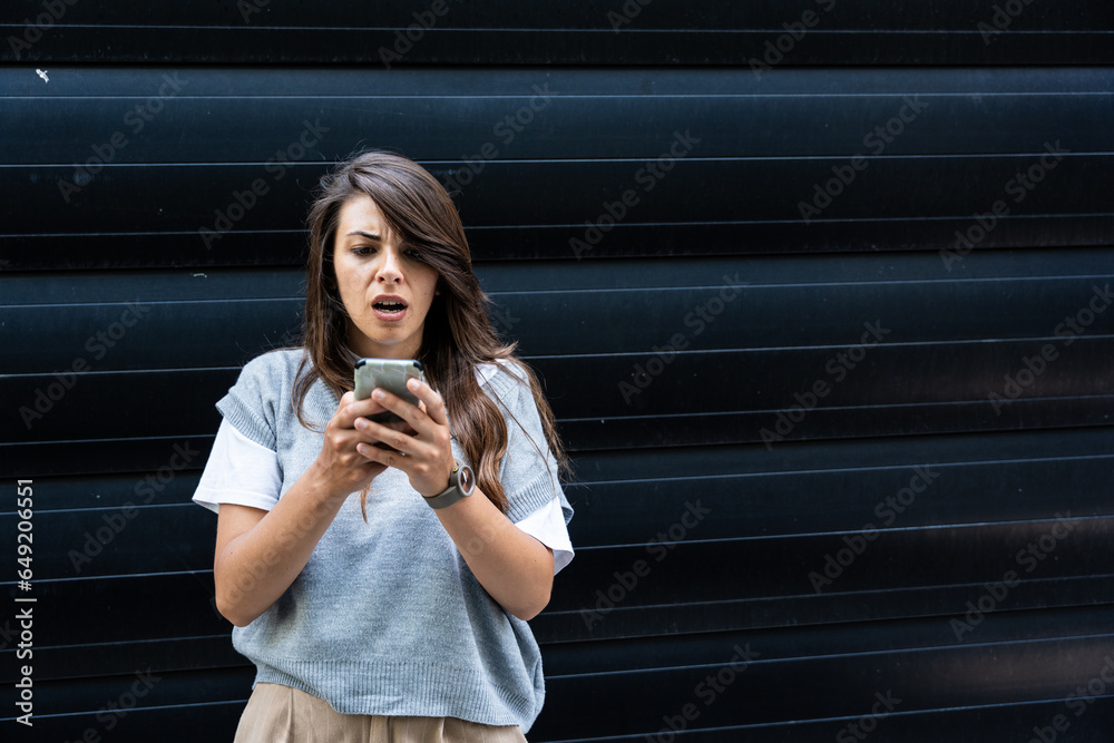 Fototapeta premium Upset and sad woman with phone in hands reading online message, Hispanic business woman received bad news notification while walking outside office building with smartphone.
