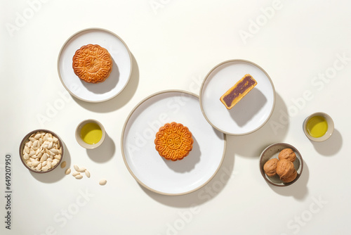 On the white background  round ceramic dishes containing mooncakes  pumpkin seeds and walnuts decorated. Creative layout for advertising mooncake product. Modern style
