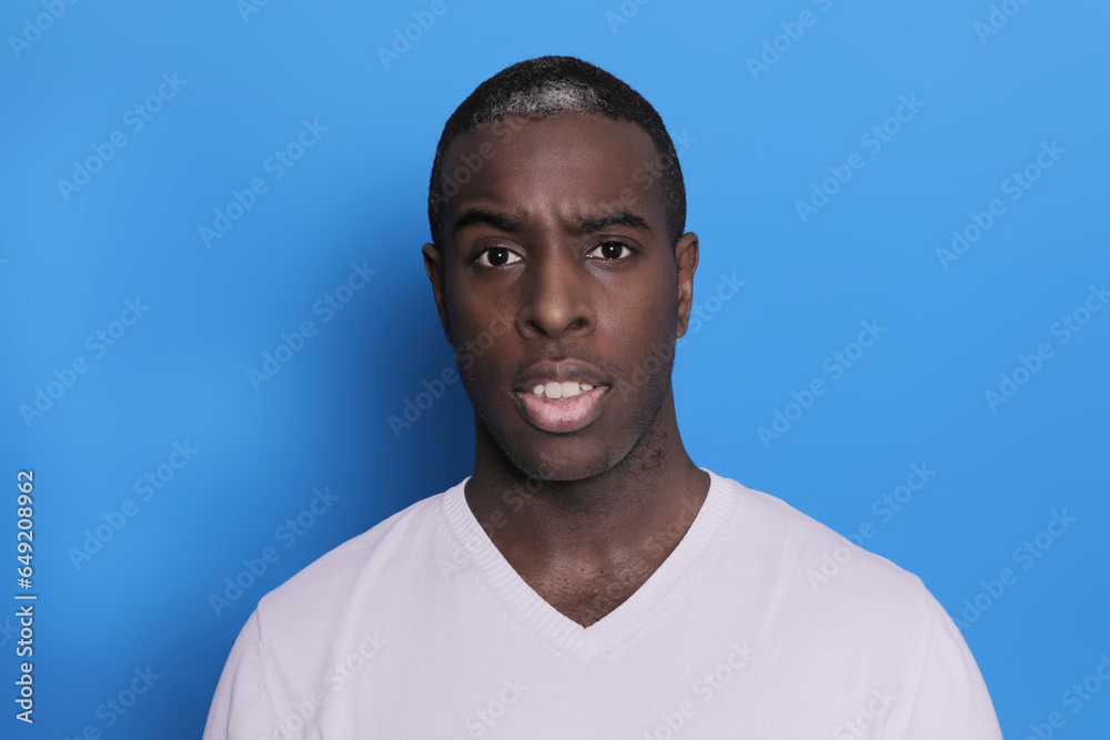 Portrait of cheerful young african-american guy wearing white casual sweater posing isolated on blue background Portrait of cheerful young african-american guy wearing white casual sweater posing isolated on blue background