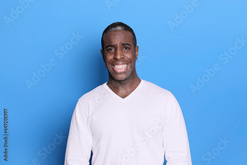 Portrait of cheerful young african-american guy wearing white casual sweater posing isolated on blue background