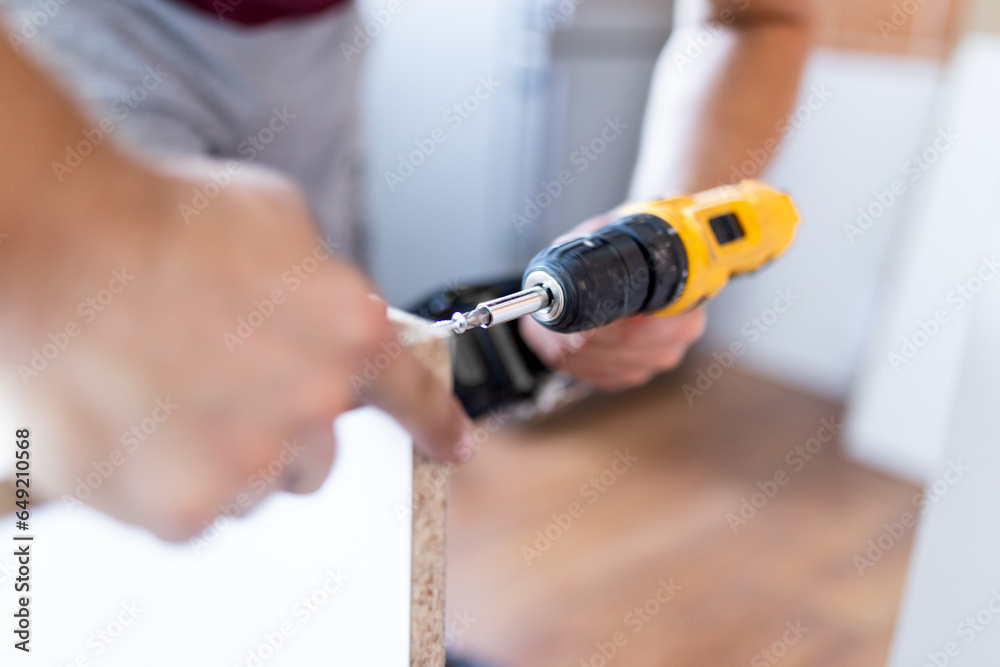 Handyman at work. Repairing kitchen shelves with cordless screwdriver