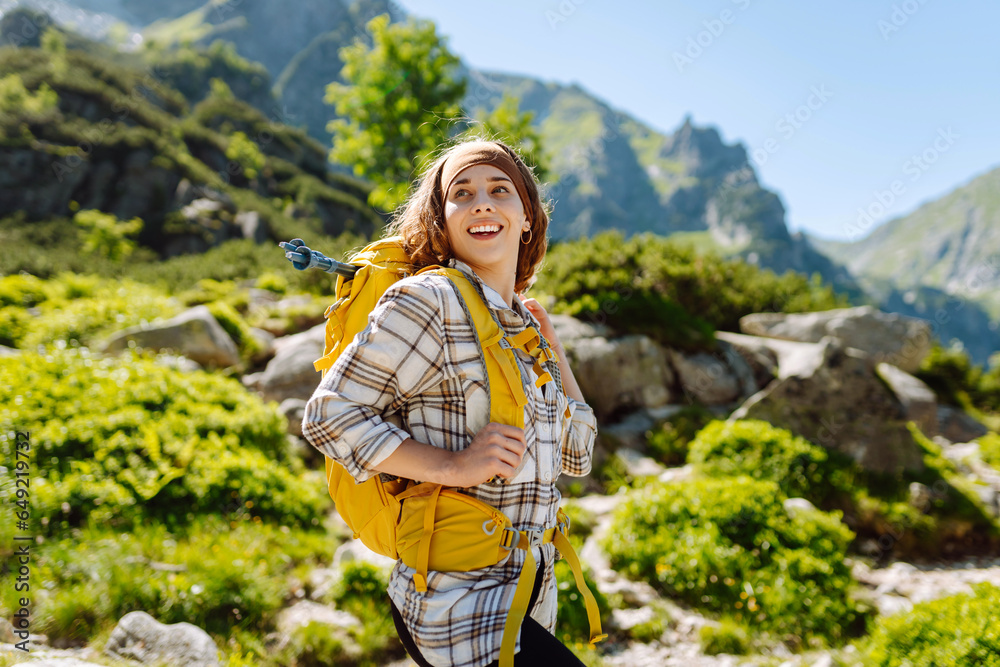Naklejka premium Portrait of a happy female traveler with a yellow hiking backpack standing on the top of a mountain. Concept of nature, sport, adventure.