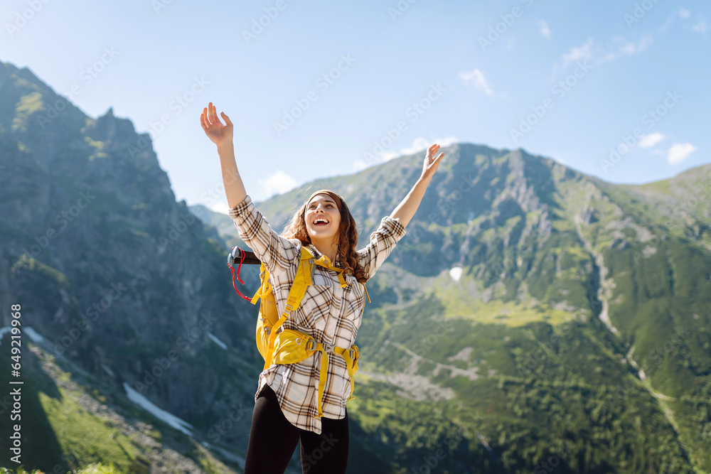 Portrait of a happy female traveler with a yellow hiking backpack standing on the top of a mountain. Concept of nature, sport, adventure.