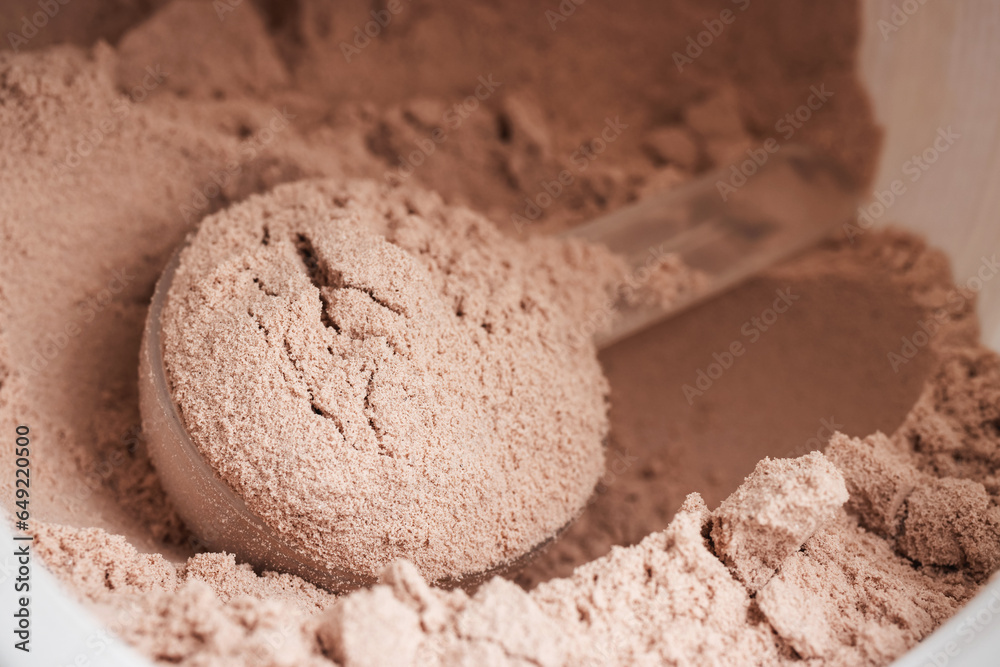 Scoop of chocolate whey protein isolate in a plastic jar, close-up view Scoop of chocolate whey protein isolate in a plastic jar, close-up view
