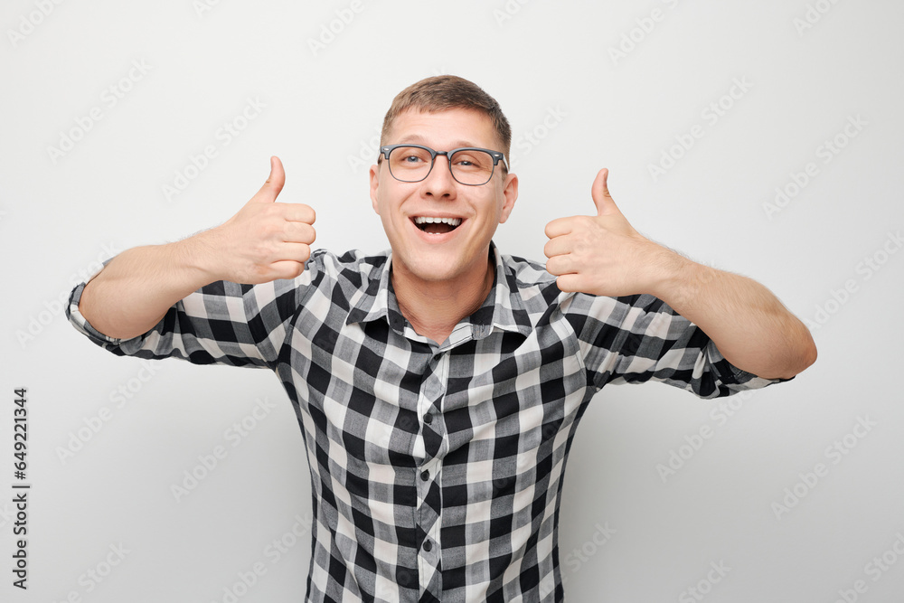 Portrait of young Caucasian man smiling joyfully showing thumbs up gesture isolated on white studio background. Approves good choice, right decision. Portrait of young Caucasian man smiling joyfully showing thumbs up gesture isolated on white studio background. Approves good choice, right decision.