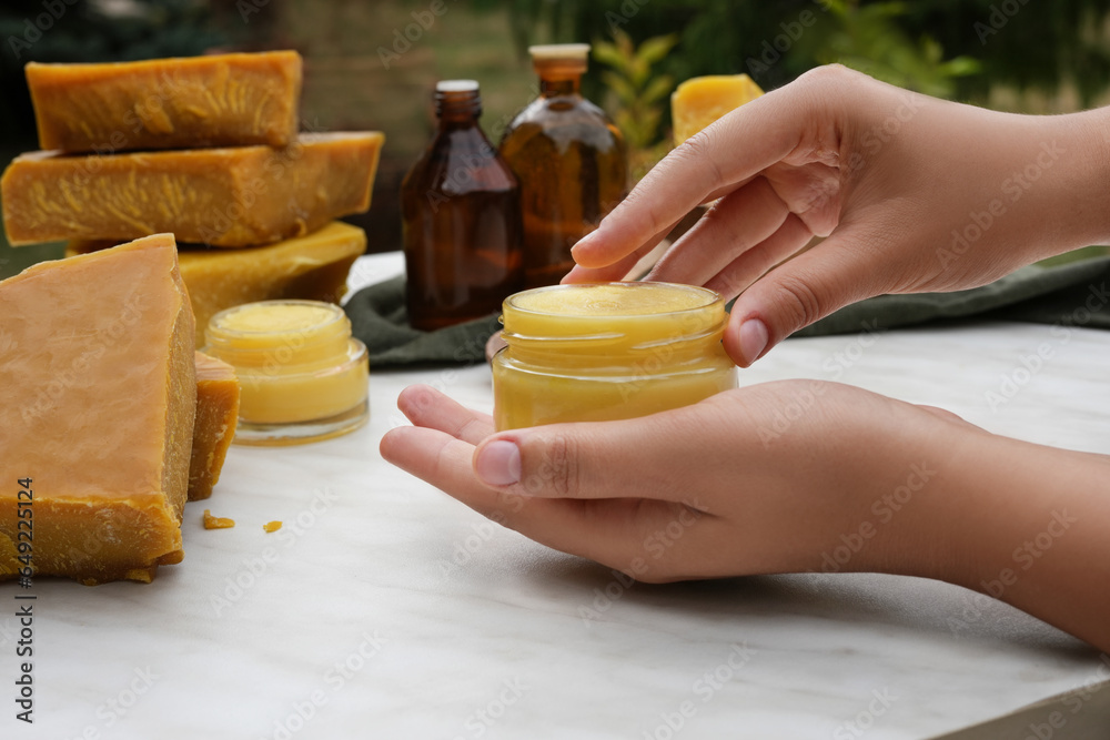 Woman hands using beeswax ointment. Medicinal cream from beeswax good for skin. Ingredients for making homemade skin cream on background. Side view. - obrazy, fototapety, plakaty 