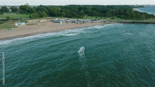 Establishing aerial view of a group of people engaged in kitesurfing, sunny summer day, high waves, extreme sport, Baltic Sea Karosta beach (Liepaja), wide drone shot moving forward