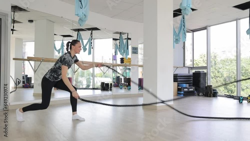 A strong woman with a toned body works out in the gym, exercising and using wavy ropes.  photo