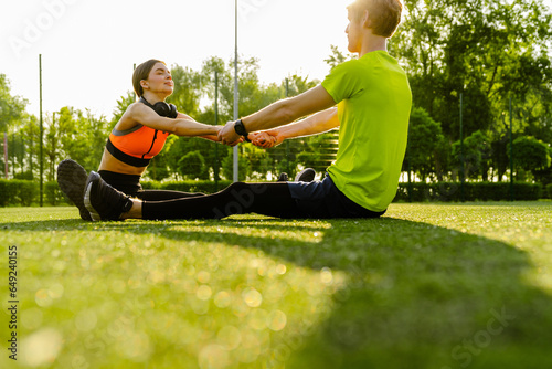 Athletic man and woman doing stretching exersises together while sitting on grass in park photo