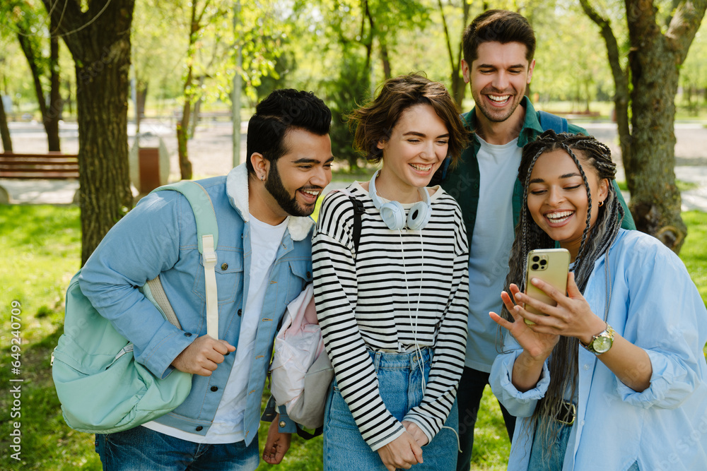 Four cheerful students taking selfie while spending time together in park Four cheerful students taking selfie while spending time together in park