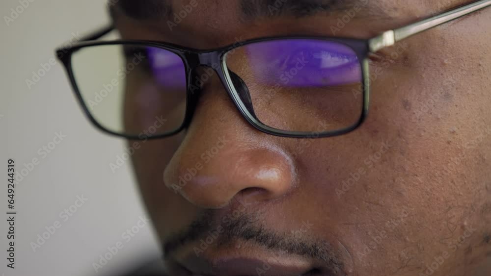 Close up view of focused Black African American businessman wears computer glasses for reducing eye strain blurred vision looking at pc screen with computer reflection using internet, reading Close up view of focused Black African American businessman wears computer glasses for reducing eye strain blurred vision looking at pc screen with computer reflection using internet, reading