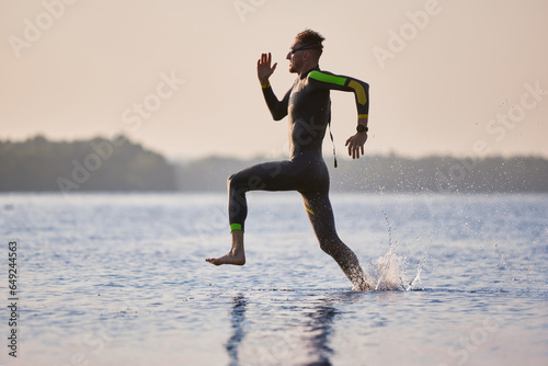 Professional triathlete, sportsman in wetsuit running into water for swimming training. Speed and endurance. Concept of professional sport, triathlon preparation, competition, athleticism