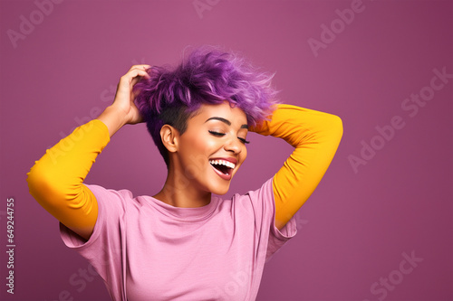Woman with short sassy purple color hair, with hands touching her hair and laughing away. On purple background, copy space. photo
