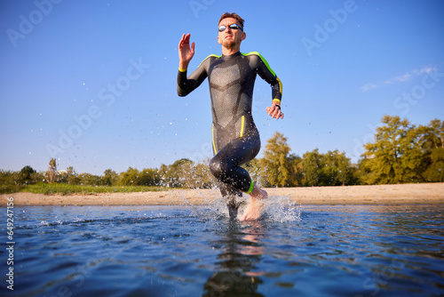 Man, sportsman in wetsuit and goggles training outdoors in morning, running into water, swimming in river. Concept of professional sport, triathlon preparation, competition, athleticism photo