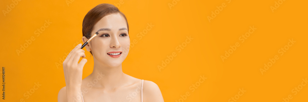 Yellow banner studio photo of a young woman using make up brush and eye shadows. Yellow banner studio photo of a young woman using make up brush and eye shadows.